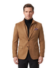 A man stands against a light gray studio background wearing a camel brown suede blazer over a black turtleneck, black trousers, and black dress shoes. A patterned pocket square is tucked into his jacket's breast pocket.